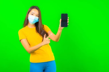 Güzel Asyalı genç bir kadının portresi, yeşil yalıtılmış arka planda kovid19 veya koronavirüsten korunmak için maske takar.