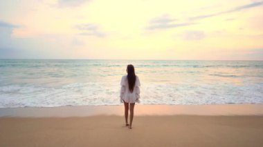 Gün batımında okyanusa bakan güzel Asyalı genç bir kadının görüntüleri.