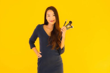 Sarı izole arkaplanda makyaj fırçası olan güzel bir Asyalı kadın portresi.