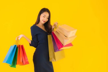 Sarı izole edilmiş arka planda renkli alışveriş çantalı güzel Asyalı kadın portresi.