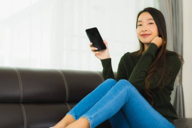 Güzel bir Asyalı kadın oturma odasındaki koltukta akıllı cep telefonu ya da cep telefonu kullanıyor.