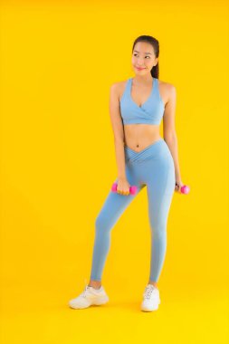 Dambıl ve spor giysili güzel Asyalı kadın sarı izole arka planda egzersize hazır.