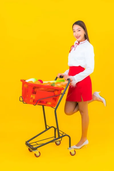 노란색 배경에 슈퍼마켓에서 식료품 바구니를 가지고 아름다운 아시아 여자의 — 스톡 사진
