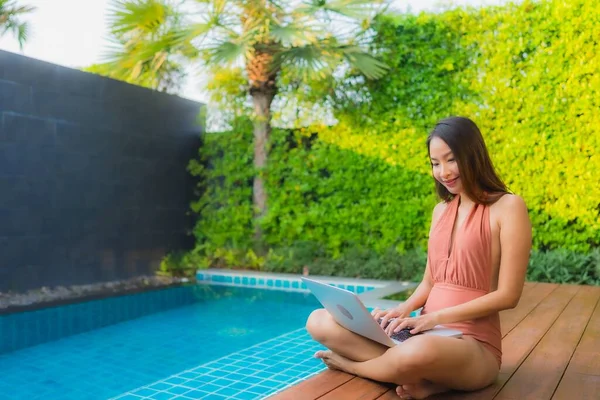 Genç Asyalı bir kadının portresi oteldeki yüzme havuzunda dizüstü bilgisayar kullanıyor.