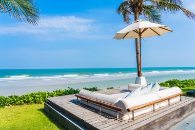 Şemsiye ve sandalye deniz kıyısında, içinde hindistan cevizi palmiyesi, mavi gökyüzü, tatil için beyaz bulut var.