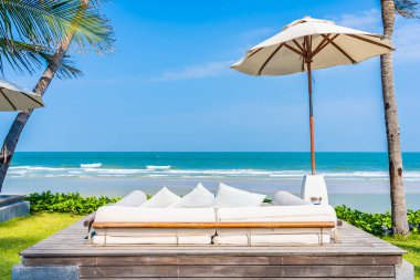 Şemsiye ve sandalye deniz kıyısında, içinde hindistan cevizi palmiyesi, mavi gökyüzü, tatil için beyaz bulut var.