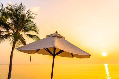 Şemsiye ve güverte sandalyesi sahil denizi çevresinde gün batımında hindistan cevizi palmiyesi ağacıyla ya da tatil için gün doğumuyla