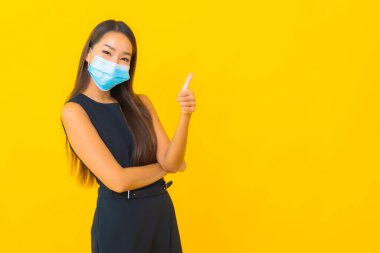 Güzel Asyalı iş kadını portresi sarı arka planda Covid19 'u korumak için maske takıyor.