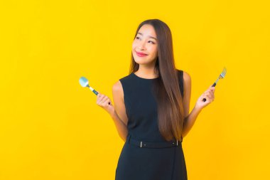 Sarı arka planda çatal ve kaşıkla yemeye hazır güzel Asyalı kadın portresi.