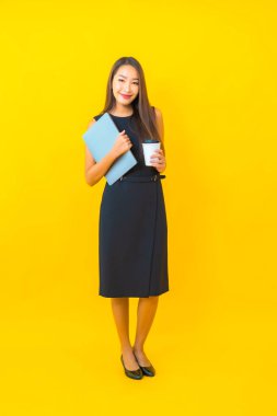 Sarı arka planda dizüstü bilgisayarı olan güzel Asyalı iş kadını portresi