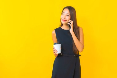 Kahve fincanı ve sarı arka planda akıllı cep telefonlu güzel Asyalı iş kadını portresi.