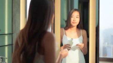 Evdeki aynanın önünde cilt bakımı yapan güzel Asyalı bir kadının görüntüsü.