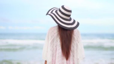 Sahilde duran şapkalı güzel Asyalı genç bir kadının görüntüleri.