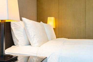 Yatak odasının içinde lamba süslemesi olan beyaz rahat yastık ve battaniye.