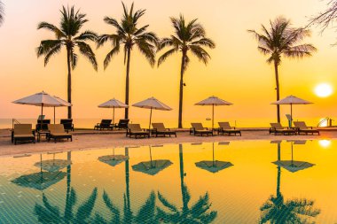 Şemsiye ve sandalye gün batımında ya da gün doğumunda deniz kıyısı okyanusu olan açık havuzda yüzer.