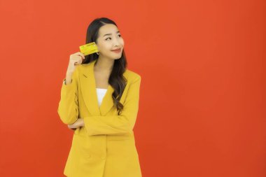 Güzel bir Asyalı kadının portresi kırmızı arka planda kredi kartıyla cep telefonu kullanıyor.