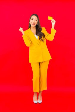 Güzel bir Asyalı kadının portresi kırmızı arka planda kredi kartıyla cep telefonu kullanıyor.