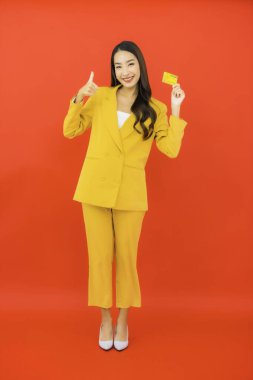 Güzel bir Asyalı kadının portresi kırmızı arka planda kredi kartıyla cep telefonu kullanıyor.