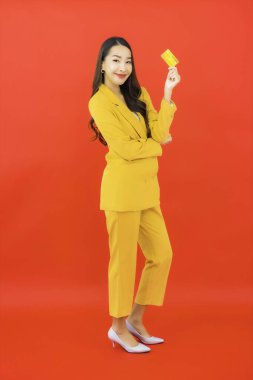 Güzel bir Asyalı kadının portresi kırmızı arka planda kredi kartıyla cep telefonu kullanıyor.