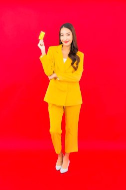 Güzel bir Asyalı kadının portresi kırmızı arka planda kredi kartıyla cep telefonu kullanıyor.