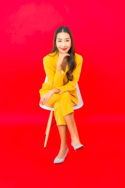 Portre güzel genç iş kadını Asyalı kadın kırmızı arka planda gülümseyerek sandalyede oturuyor.