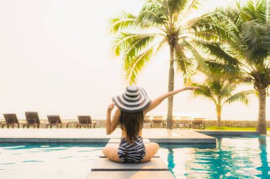Güzel bir Asyalı kadın portresi, gün batımında palmiye ağacıyla birlikte havuz kenarında dinleniyor ya da tatil için gün doğumunda dinleniyor.