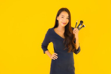 Sarı izole arkaplanda makyaj fırçası olan güzel bir Asyalı kadın portresi.