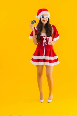 Güzel bir Asyalı kadın portresi patlamış mısır ve 3D gözlüklü noel şapkası takıyor sarı izole edilmiş arka planda film izlemeye hazır.