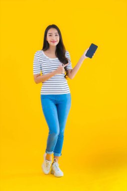 Güzel Asyalı genç bir kadının portresi mutlu bir gülümseme sarı izole edilmiş arka planda akıllı cep telefonu kullanın