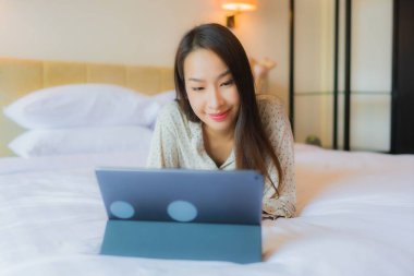 Güzel bir Asyalı kadının portresi yatak odasının içinde kredi kartıyla tablet kullanıyor.