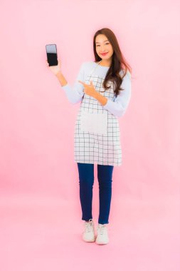 Güzel bir Asyalı kadın pembe izole edilmiş arka planda akıllı cep telefonu kullanıyor.