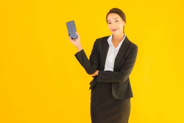 Portre güzel genç Asyalı kadın akıllı cep telefonu ve kahve fincanı ile izole edilmiş sarı arka planda