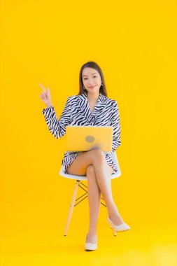 Güzel bir Asyalı kadın, sarı izole edilmiş arka planda dizüstü bilgisayar kullanıyor.