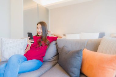 Güzel bir Asyalı kadın portresi. Yatak odasının iç tarafındaki oturma odasındaki koltukta akıllı cep telefonu kullanıyor.