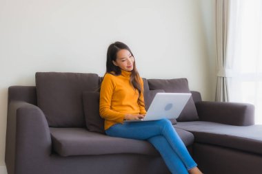 Genç Asyalı bir kadının oturma odasında çalışmak için dizüstü bilgisayar defteri kullanmasının portresi.