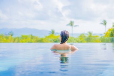 Güzel bir Asyalı kadın portresi gezide deniz manzaralı açık havuzda yüzüyor.