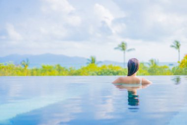 Güzel bir Asyalı kadın portresi gezide deniz manzaralı açık havuzda yüzüyor.