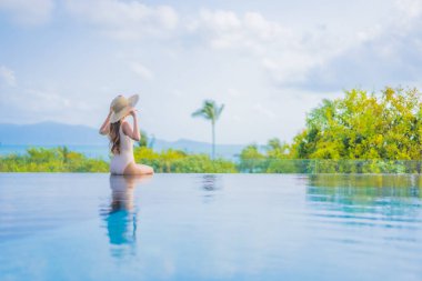 Güzel bir Asyalı kadın portresi gezide deniz manzaralı açık havuzda yüzüyor.