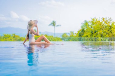 Güzel bir Asyalı kadın portresi gezide deniz manzaralı açık havuzda yüzüyor.