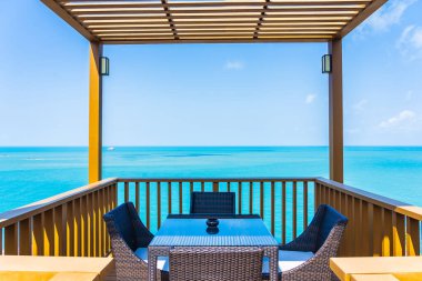 Boş sandalyeli açık hava terası ve beyaz bulutlu mavi gökyüzü manzaralı deniz manzaralı bir masa.