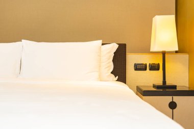 Yatak odasının içinde lamba süslemesi olan beyaz rahat yastık ve battaniye.