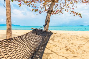 Boş hamak deniz kıyısında sallanıyor. Beyaz bulutlu mavi gökyüzü seyahat için.