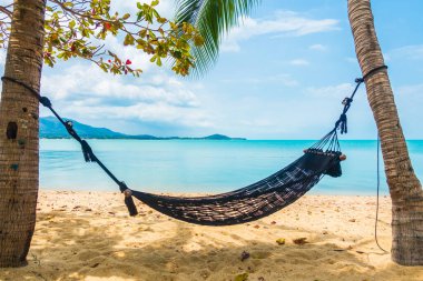 Boş hamak deniz kıyısında sallanıyor. Beyaz bulutlu mavi gökyüzü seyahat için.