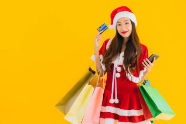 Güzel bir Asyalı kadın portresi. Sarı izole edilmiş arka planda bir sürü alışveriş çantasıyla noel şapkası takıyor.