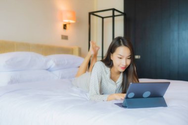 Güzel bir Asyalı kadının portresi yatak odasının içinde kredi kartıyla tablet kullanıyor.