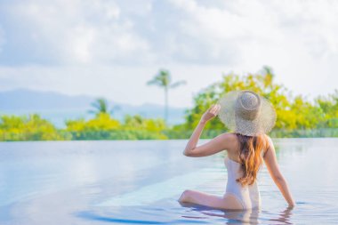 Güzel bir Asyalı kadın portresi gezide deniz manzaralı açık havuzda yüzüyor.