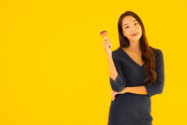 Sarı izole arkaplanda makyaj fırçası olan güzel bir Asyalı kadın portresi.