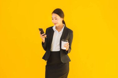 Portre güzel genç Asyalı kadın akıllı cep telefonu ve kahve fincanı ile izole edilmiş sarı arka planda