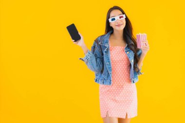 Güzel bir Asyalı kadın portresi telefon patlamış mısırı ve sarı izole edilmiş bir arka planda film izlemekten memnun.