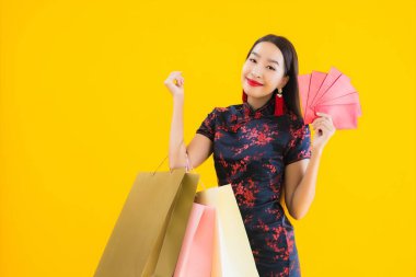 Güzel bir Asyalı kadın portresi Çin elbisesi giyer alışveriş çantası, akıllı cep telefonu, Çin yeni yılı için kredi kartı sarı izole arka planda.